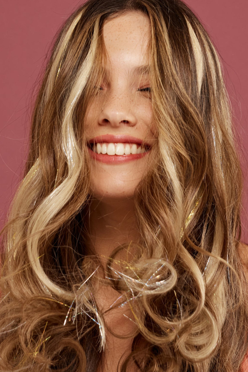 קלוז אפ של בחורה שבשיער שלה שזורים גווני שיער טבעיים, גליים, בצבע בלונד פלטינה - תוספות השיער מעורבבות עם גווני פיות כסופים וזהובים ומיועדות לחיבור עצמאי, פשוט  וקבוע לשיער או לחיבור זמני - Shufizoo לשיער