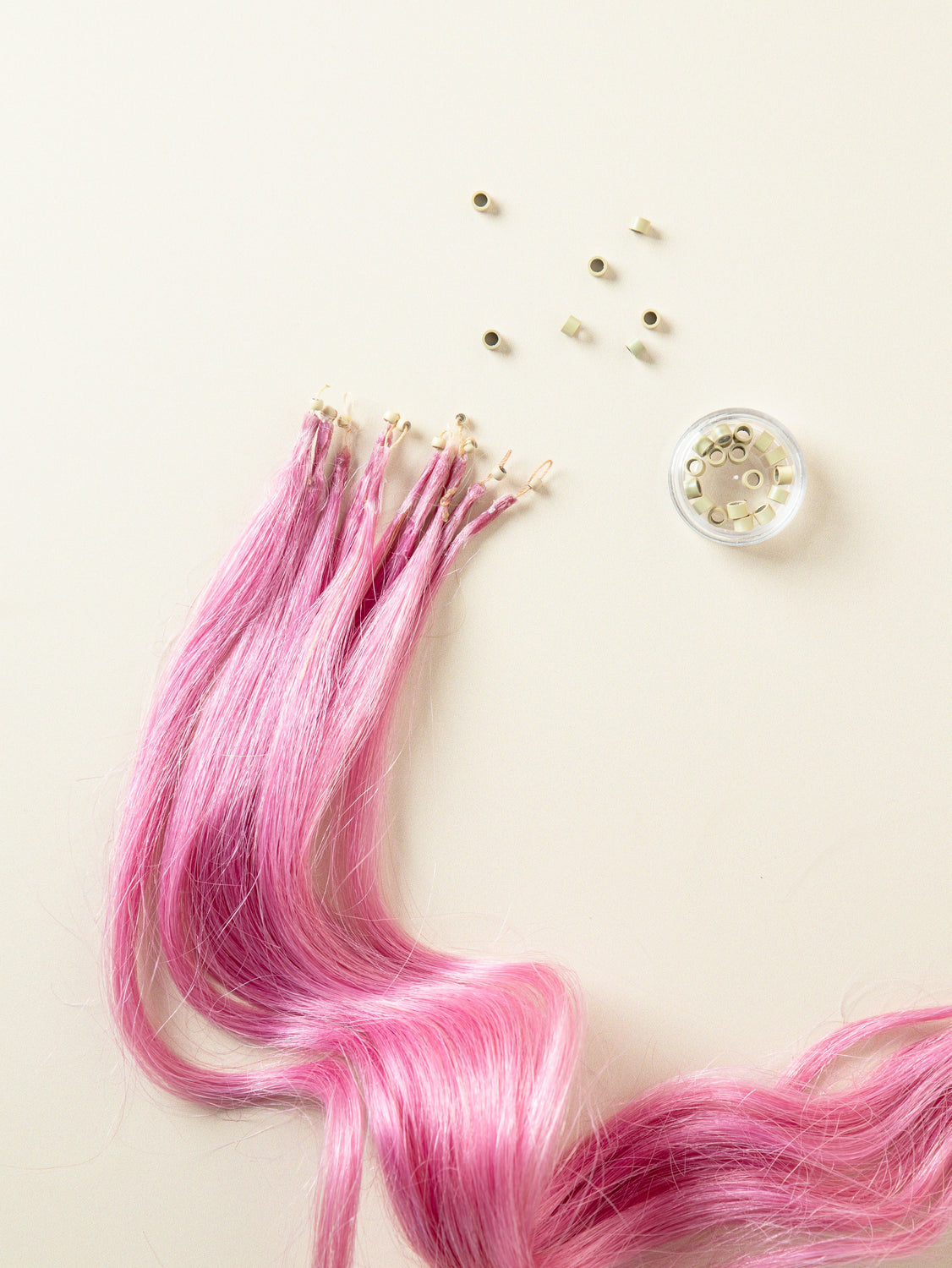 פקשוט של תוספות שיער טבעיות, במרקם חלק - בצבע מג'נטה. ליד התוספות יש חרוזי מעיכה לוספות שיער, בצבע בלונדיני